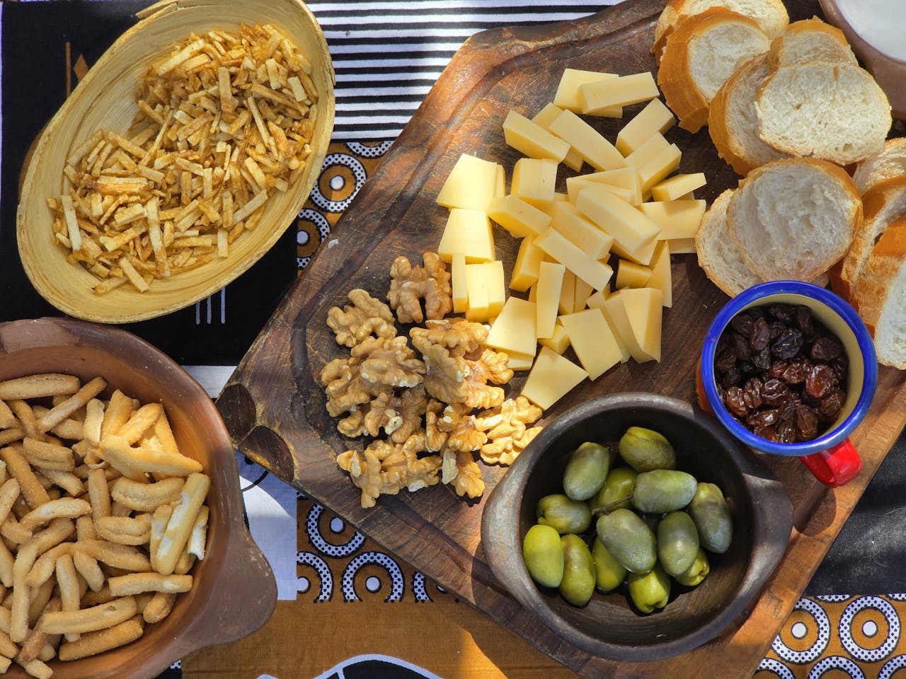 A rustic picnic spread featuring cheese, nuts, olives, and bread on a wooden board.
